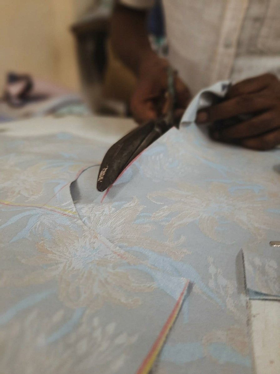 A Black Lapel tailor cutting floral jacquard cloth with shears
